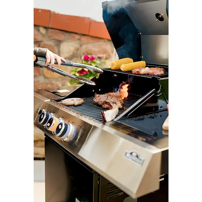 Kingstone Grillzange - Länge: 46 cm - Bild von einem Grill mit Steaks, Mais und einer Wurst. Die Steaks brutzeln und eine Hand hält eine Zange über das Essen.