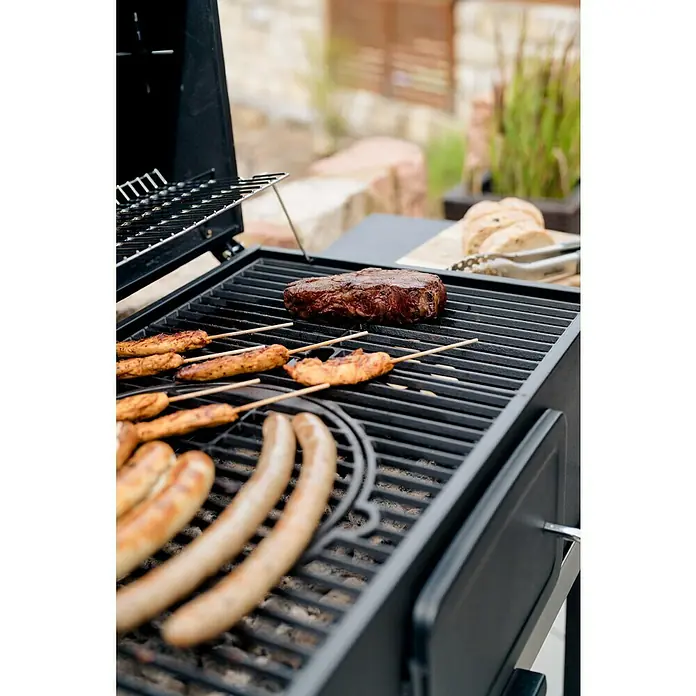 Kingstone KMS Holzkohlegrill Black Angus XXL - Grillfläche (B x T): 70 x 43,5 cm, Schwarz - Nahaufnahme eines Grills mit Würstchen, Hähnchenspießen und einem Steak, die darauf zubereitet werden. Köstliches Essen im Freien.