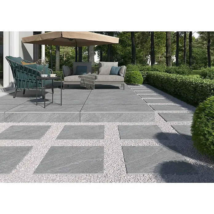 Terrassenfliese Piazza 2.0 - 59,7 x 59,7 x 2 cm, Grau, Matt - Terrasse mit grauen Fliesen und weißen Kieselsteinen. Gartenmöbel unter einem Sonnenschirm sorgen für Komfort im Freien.
