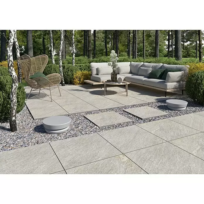 Terrassenfliese Piazza 2.0 - 59,7 x 59,7 x 2 cm, Sabbia, Matt - Helle Outdoor-Pflasterplatten bilden eine Terrasse und einen Weg mit Zierkies in einer Gartenumgebung.