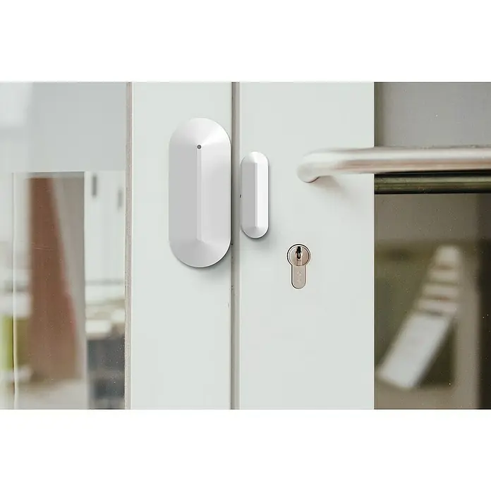 Safe2Home Fenstersensor SP310 - Passend für: Safe2Home Alarmanlage SP310, Reichweite ca.: 400 m - Nahaufnahme eines weißen Tür- und Fenstersensors an einer Tür, der Sicherheit und Schutz bietet.