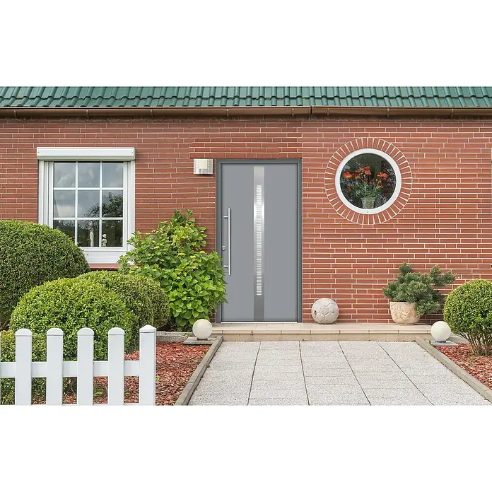 Splendoor Haustür Thermodoor PLUS SP20 - 100 x 210 cm, DIN Anschlag: Links, Verkehrsgrau - Fassade eines Hauses mit grauer Tür, rundem Fenster und weißem Fenster, umgeben von üppigem Grün und einem weißen Zaun.