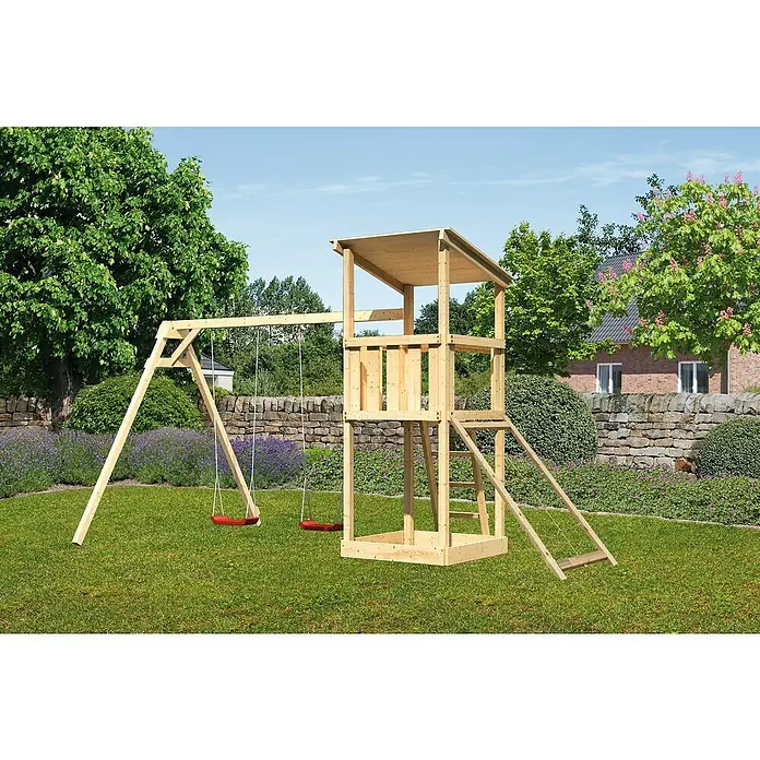 Karibu Kinderspielturm Anna Set 21 - L x B x H: 264 x 347 x 270 cm, Natur - Holzspielturm mit Schaukel und Rutsche im Garten mit Mauer im Hintergrund. Ideal für Kinder zum Spielen im Freien.