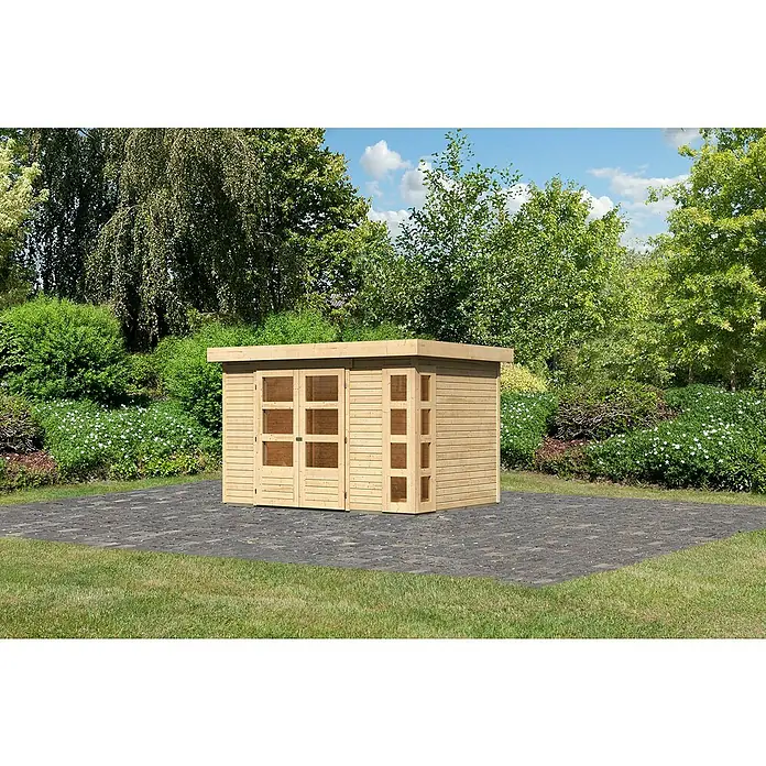 Karibu Gartenhaus Kerko 4 - Außenmaß inkl. Dachüberstand (B x T): 330 x 238 cm, Holz, Natur - Ein helles Holzgartenhaus mit Fenstern steht auf einer gepflasterten Fläche, umgeben von üppigem Grün. Das Haus bietet Stauraum im Freien.