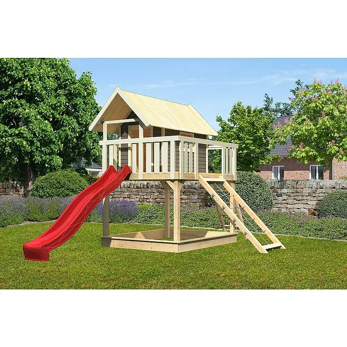 Karibu Kinderspielturm Fidel Set 14 - L x B x H: 243 x 198 x 329,5 cm, Terragrau/Rot - Ein hölzernes Spielhaus mit roter Rutsche, Leiter und Sandkasten, umgeben von Grün, bietet Kindern Spaß und Abenteuer im Freien.