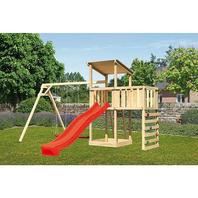 Karibu Kinderspielturm Anna Set 52 - L x B x H: 264 x 454 x 270 cm, Natur - Ein hölzernes Spielhaus mit Rutsche, Schaukel und Kletterwand steht im Garten, umgeben von Grün und Bäumen.