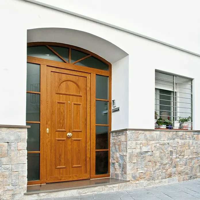 Revestimiento de piedra Alpes Pino - Cantidad total: 4 pzs. - Puerta principal marrón con paneles de vidrio y arco decorativo, integrada en una fachada blanca con elementos de piedra.