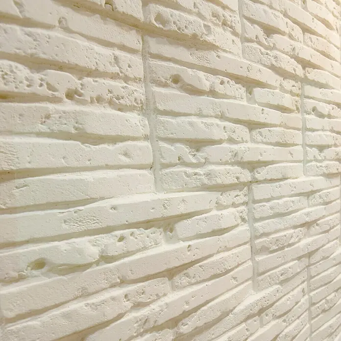 Revestimiento de piedra Listelo Hueso - 28 x 14 x 1 cm - Primer plano de una pared de ladrillo blanco. Los ladrillos tienen una forma irregular y una textura rugosa, dando al ladrillo un aspecto rústico.