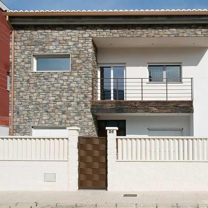 Revestimiento de piedra Silleria Plomo - Gris, Cantidad total: 4 pzs. - Fachada de una casa moderna con pared de piedra, balcón y puerta marrón.