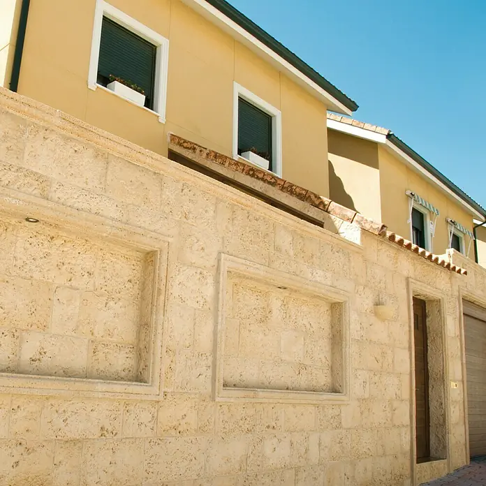 Revestimiento de piedra Coral Piedra - Coral - Fachada de un edificio con un muro hecho de bloques de piedra natural de travertino, que aporta una estética y textura cálida y natural.