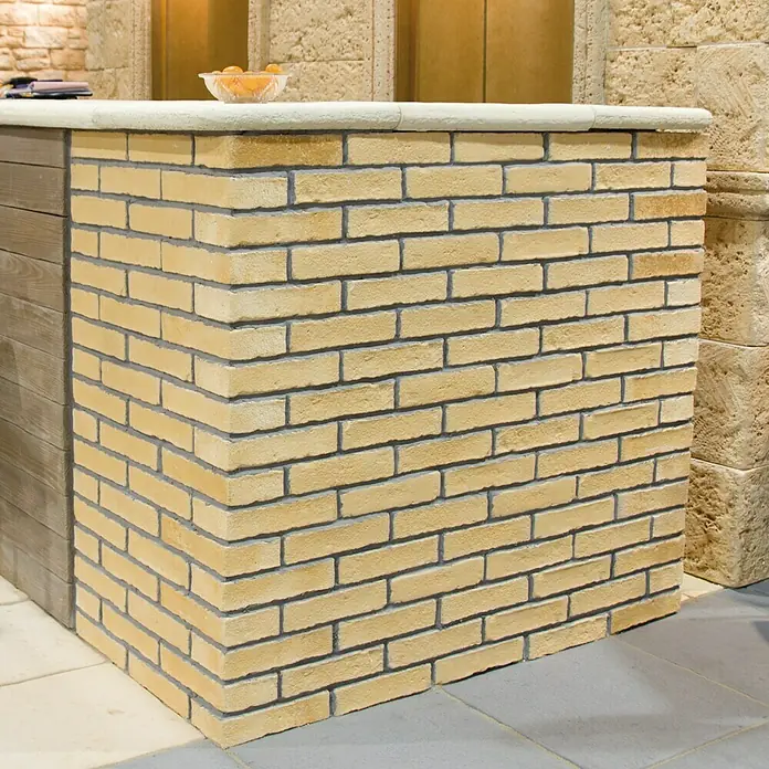 Revestimiento de piedra Mediterráneo Barro - 24 x 5,5 x 2,5 cm - Un primer plano de un mostrador de ladrillo con detalles de madera y una tapa blanca, con un frutero encima.