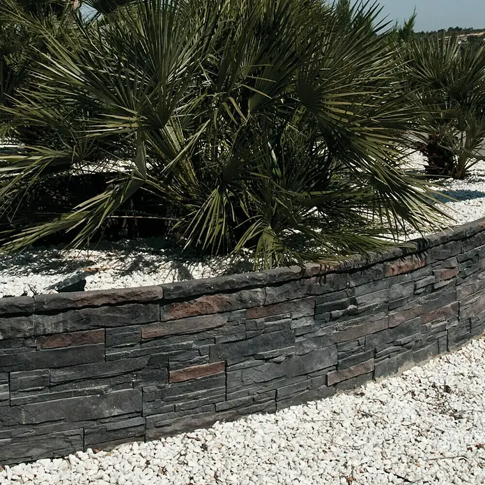 Revestimiento de piedra Petra Onix - Cantidad total: 4 pzs., Onix - Primer plano de un muro de piedra curvo decorativo con plantas y guijarros blancos, ideal para el diseño de jardines y el paisajismo.