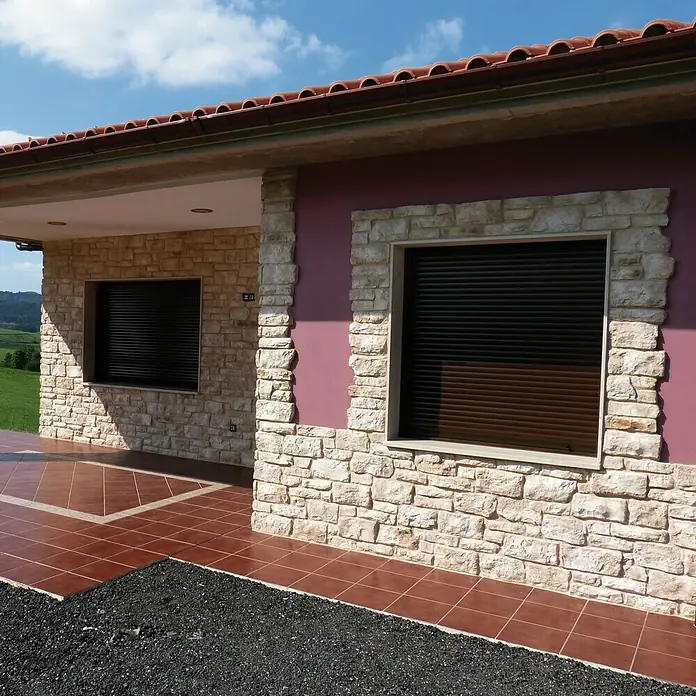 Revestimiento de piedra Silleria Cobre - Cobre, Cantidad total: 4 pzs. - Primer plano de una casa con techo de ladrillo rojo, persianas y mampostería de piedra. El exterior de la casa combina color y textura.