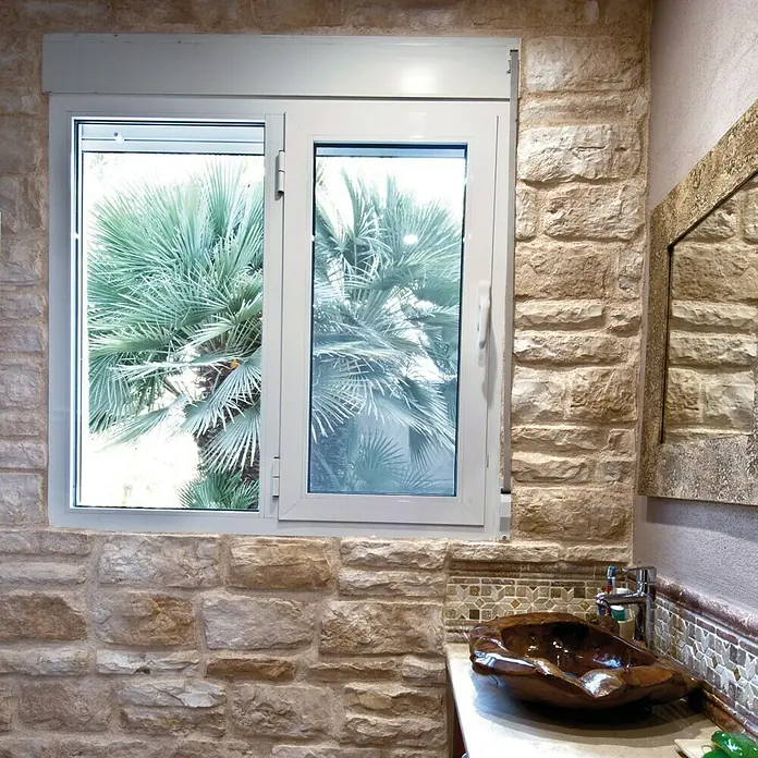 Revestimiento de piedra Silleria Cobre - Cobre, Cantidad total: 4 pzs. - Luminosa ventana de baño con vista a una palmera, ubicada en una pared de piedra rústica sobre un lavabo de madera único.