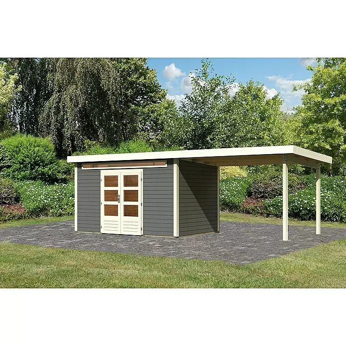 Karibu Gartenhaus Kandern 7 - Außenmaß inkl. Dachüberstand (B x T): 702 x 273 cm, Holz, Terragrau, Mit Seitendach - Dunkelgrauer Geräteschuppen mit cremefarbenen Akzenten und angebautem Carport auf gepflasterter Fläche im Garten.