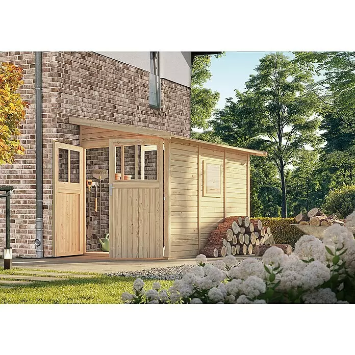 Karibu Gartenhaus Wandlitz 3 - Außenmaß inkl. Dachüberstand (B x T): 200 x 320 cm, Holz, Natur - Helles Holzgartenhaus mit offenen Doppeltüren und Fenster, neben einem Backsteinhaus mit gestapeltem Brennholz.