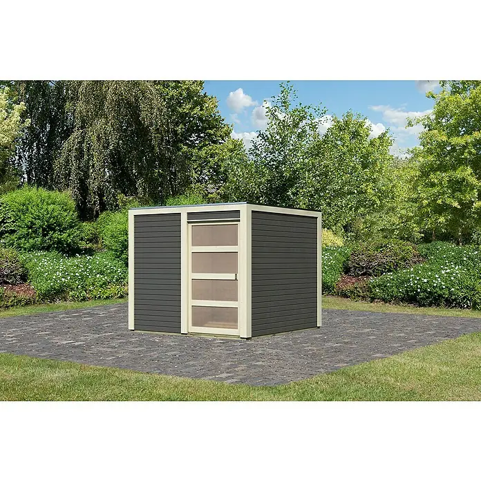 Karibu Gartenhaus Qubic 1Außenmaß inkl. Dachüberstand (B x T): 246 x 246 cm, Holz, Terragrau - Ein modernes Gartenhaus mit einer grauen Holzverkleidung und einer Tür mit transparenten Paneelen steht auf einer gepflasterten Fläche im Garten.