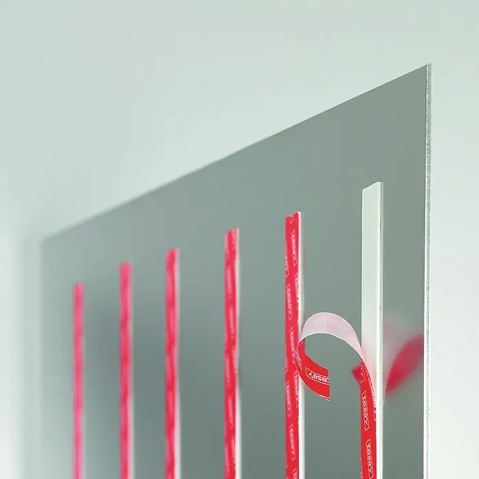 Tesa Cinta adhesiva de papel Powerbond Ultra Fuerte - 5 m x 19 mm - Primer plano de una tabla con tiras adhesivas de montaje Tesa Powerstrips, con la película protectora roja parcialmente despegada.
