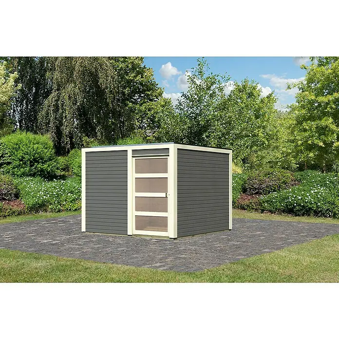Karibu Gartenhaus Qubic 2 - Außenmaß inkl. Dachüberstand (B x T): 276 x 276 cm, Holz, Terragrau - Diese Aufnahme zeigt ein Gartenhaus mit einer Tür mit vier Paneelen auf einer gepflasterten Fläche, umgeben von grüner Vegetation.