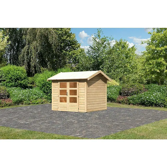 Karibu Gartenhaus Theres - Außenmaß inkl. Dachüberstand (B x T): 270 x 288 cm, Holz, Natur - Ein Holzschuppen mit Doppeltüren und einem hellen Dach steht auf Pflastersteinen, umgeben von üppigem Grün. Ideal zur Gartenaufbewahrung.