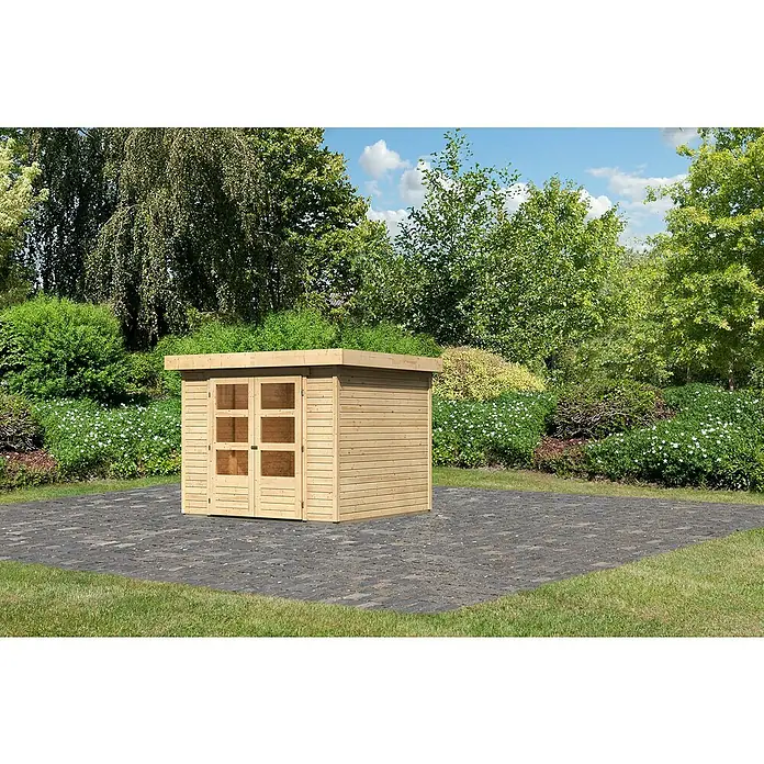 Karibu Gartenhaus Cuno 3 - Außenmaß inkl. Dachüberstand (B x T): 266 x 262 cm, Holz, Natur - Ein Holzschuppen mit Flachdach und Doppeltür steht auf einem gepflasterten Bereich im Garten, umgeben von Grün.