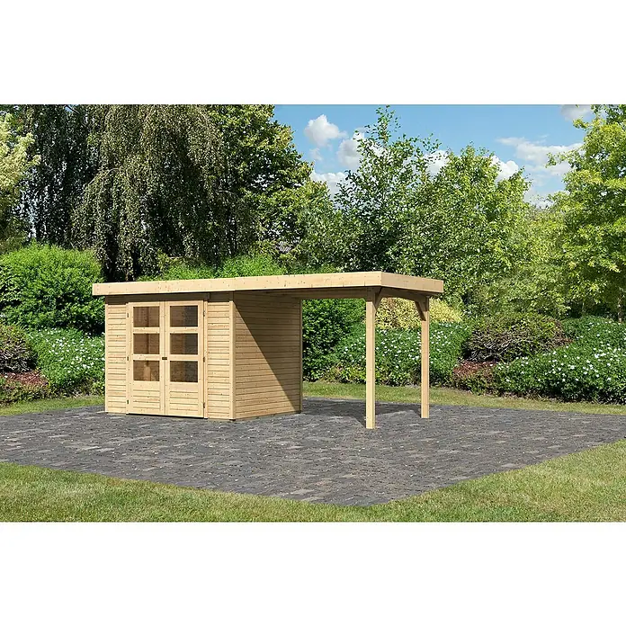 Karibu Gartenhaus Cuno 2 - Außenmaß inkl. Dachüberstand (B x T): 491 x 238 cm, Holz, Natur, Mit Seitendach - Ein helles Holzgartenhaus mit Anbau auf einer gepflasterten Fläche, umgeben von üppigem Grün. Das Gartenhaus bietet Stauraum und Schutz.