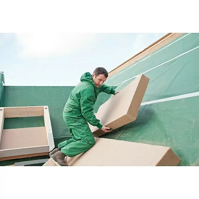 Steico Holzfaserdämmplatte therm dry - 1.350 x 600 x 60 mm, Wärmeleitfähigkeit: 0,037 W/(mK) - Mann installiert beige Dämmplatten aus Naturfasern auf einer grün abgedeckten Gebäudestruktur zur Wärmedämmung.