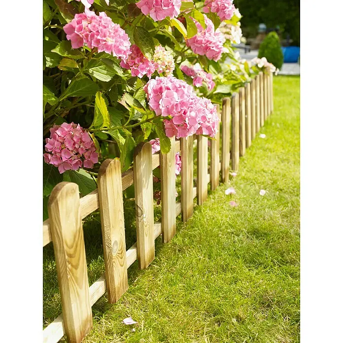 Cerland Valla mini ranurada - Natural, An x Al: 1,14 x 0,45 m - Una cerca de madera linda bordea un jardín exuberante con arbustos de hortensias rosadas, agregando encanto al paisaje.