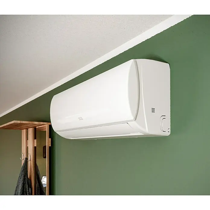 TCL Inverter-Klimasplitgerät mit Quick Connector TAC-12CHSD/TPG11 QC - Kühlleistung: 1.500 W - 3.770 W, Heizleistung: 3.810 W, Raumgröße: 35 m², Passend für: Räume bis ca. 35 m² - Nahaufnahme einer weißen TCL-Klimaanlage an einer grünen Wand, die für eine moderne und komfortable Raumklimatisierung sorgt.