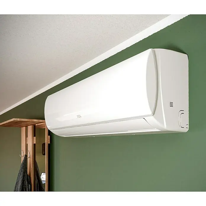 TCL Inverter-Klimasplitgerät TAC-24CHSD/TPG11 - Kühlleistung: 2.800 W - 7.820 W, Heizleistung: 7.960 W, Raumgröße: 70 m², Passend für: Räume bis ca. 70 m² - Ein weißes TCL Klimagerät ist an einer grünen Wand montiert. Das Gerät ist modern und schlank gestaltet.