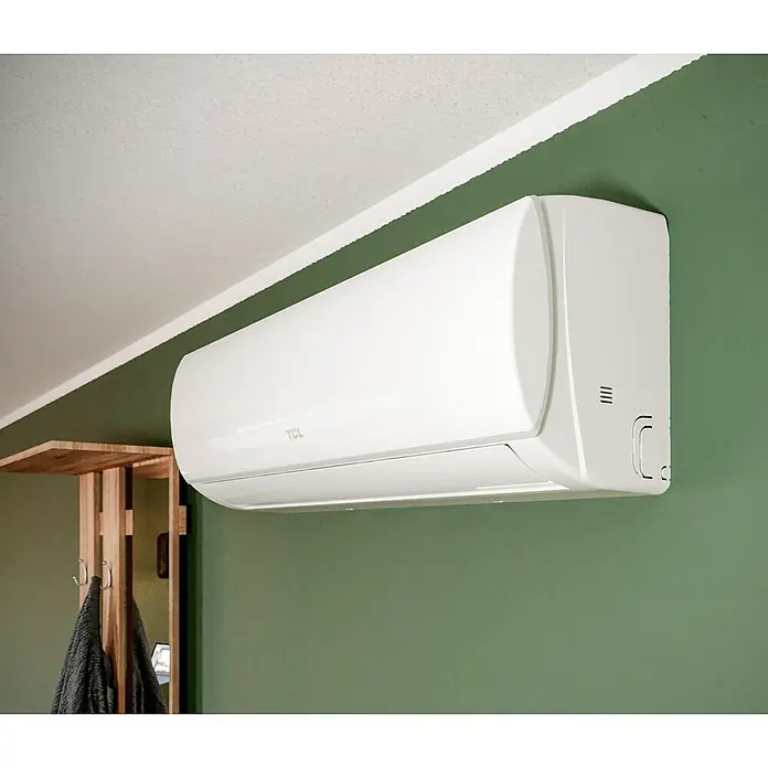 TCL Inverter-Klimasplitgerät TAC-18CHSD/TPG11 - Kühlleistung: 2.350 W - 5.900 W, Heizleistung: 6.080 W, Raumgröße: 52 m², Passend für: Räume bis ca. 52 m² - Nahaufnahme einer TCL-Klimaanlage an einer grünen Wand.