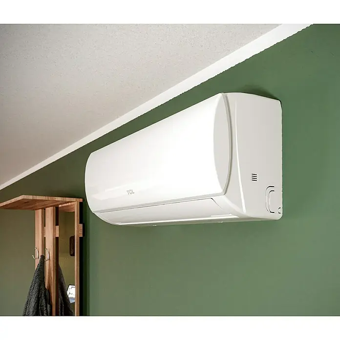 TCL Inverter-Klimasplitgerät TAC-09CHSD/TPG11 - Kühlleistung: 1.380 W - 3.300 W, Heizleistung: 3.360 W, Raumgröße: 26 m², Passend für: Räume bis ca. 26 m² - Weiße TCL Klimaanlage an einer grünen Wand montiert. Das Gerät ist modern und kompakt.