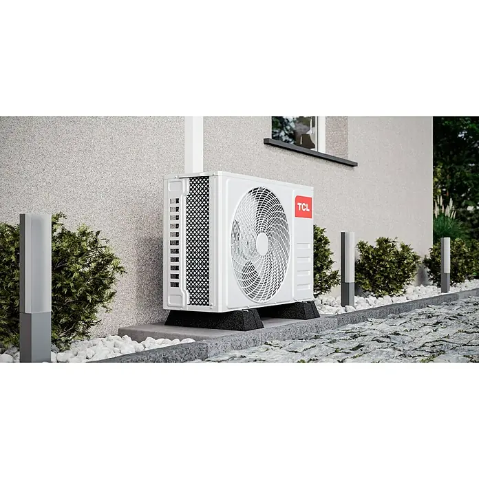 TCL Inverter-Klimasplitgerät mit Quick Connector TAC-12CHSD/TPG11 QC - Kühlleistung: 1.500 W - 3.770 W, Heizleistung: 3.810 W, Raumgröße: 35 m², Passend für: Räume bis ca. 35 m² - Ein TCL-Klimagerät steht vor einer Hauswand. Das Gerät ist weiß und hat ein rotes TCL-Logo. Es steht auf schwarzen Füßen und ist umgeben von Pflanzen.