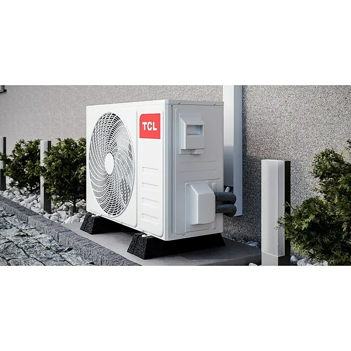 TCL Inverter-Klimasplitgerät mit Quick Connector TAC-12CHSD/TPG11 QC - Kühlleistung: 1.500 W - 3.770 W, Heizleistung: 3.810 W, Raumgröße: 35 m², Passend für: Räume bis ca. 35 m² - Außenansicht einer TCL-Klimaanlage, die auf einem Betonsockel mit umgebenden Büschen und Steinen steht und eine effiziente Kühlung im Freien bietet.
