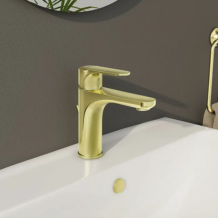 VitrA Waschtischarmatur Root Round - Gold - Nahaufnahme eines goldenen Waschtischhahns auf einem weißen Waschbecken mit einer grauen Wand im Hintergrund.