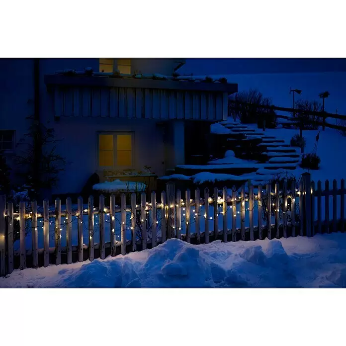 Tween Light LED-Lichterkette - Außen, Lichtfarbe: Warmweiß, Anzahl Leuchtmittel: 400 Stk., Netzbetrieben, 65 m - Warmweiße Lichterkette beleuchtet einen schneebedeckten weißen Zaun bei Nacht.