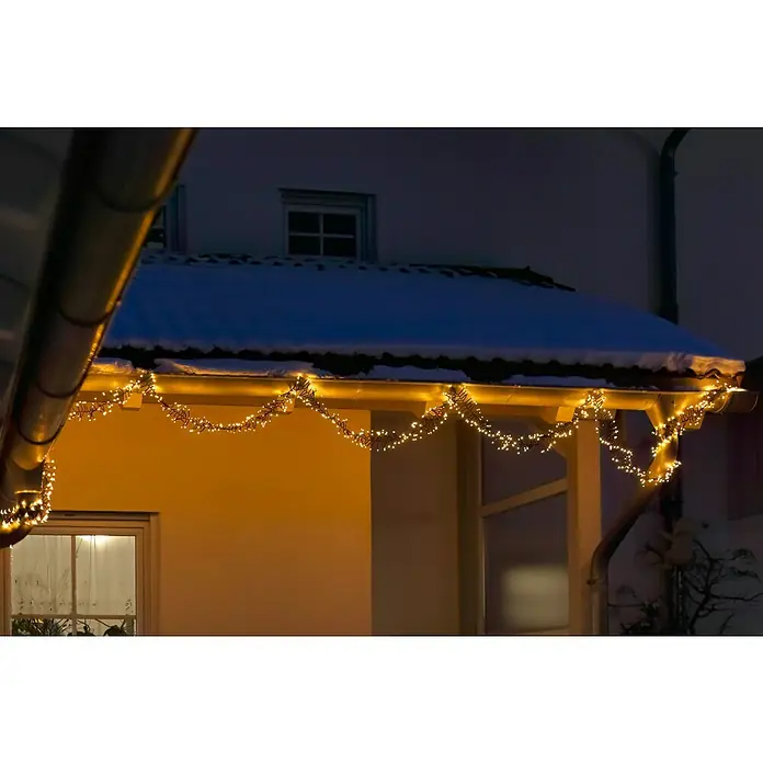 Tween Light Cadena de luces LED - Para exterior, Largo: 19,8 m, 2.000 ud., Funcionamiento en red, Color de luz: Blanco cálido - Luces decorativas adornan el techo de una casa en invierno, iluminando la noche oscura con un brillo cálido.