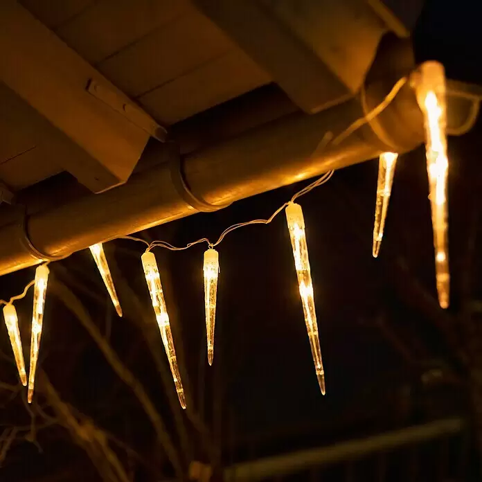 Konstsmide LED-Lichtervorhang Eiszapfen - Außen, 13,75 m, Bernstein, 24 Stk., Netzbetrieben - Warm leuchtende Eiszapfen-Lichterkette hängt nachts an einer Dachrinne.