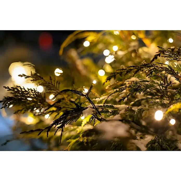 Tween Light LED-Lichterkette - Außen, Lichtfarbe: Warmweiß, Anzahl Leuchtmittel: 200 Stk., Netzbetrieben, 35 m - Festliche Weihnachtsstimmung: Nahaufnahme von beleuchteten Tannenzweigen mit zarten Schneeflocken, die eine warme und besinnliche Atmosphäre erzeugen.