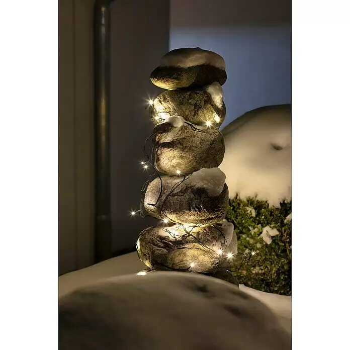LED-Lichterkette - Außen, 15 m, Lichtfarbe: Warmweiß, Anzahl Leuchtmittel: 192 Stk., Batteriebetrieben - Stapel schneebedeckter Dekosteine, umwickelt mit warmweißen Lichterketten, im winterlichen Außenbereich.