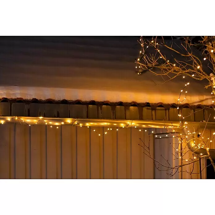 LED-Lichterkette - Außen, 15 m, Lichtfarbe: Warmweiß, Anzahl Leuchtmittel: 192 Stk., Batteriebetrieben - Warmweiße Lichterkette beleuchtet eine verschneite Dachtraufe und kahle Äste bei Nacht.