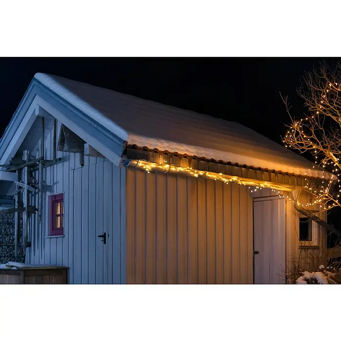 Guirnalda luminosa LED - Para exterior, 15 m, Color de luz: Blanco cálido, Número de bombillas: 192 ud., Funciona con pilas - Cabaña de invierno con luces de cadena que brillan cálidamente. La nieve cubre el techo, creando un ambiente navideño acogedor.