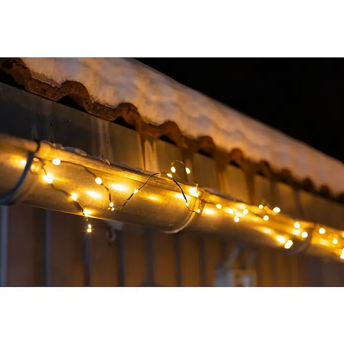 Guirnalda luminosa LED - Para exterior, 15 m, Color de luz: Blanco cálido, Número de bombillas: 192 ud., Funciona con pilas - Luces parpadeantes adornan un canalón cubierto de nieve, creando una escena invernal festiva con un brillo cálido y acogedor.