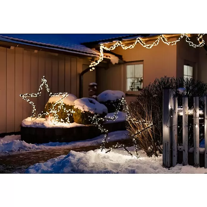 LED-Gartenstecker Stern L - Außen, Netzbetrieben, Höhe: 135 cm, Warmweiß - Warme weiße Weihnachtsbeleuchtung ziert ein verschneites Haus und Sterne im Garten.
