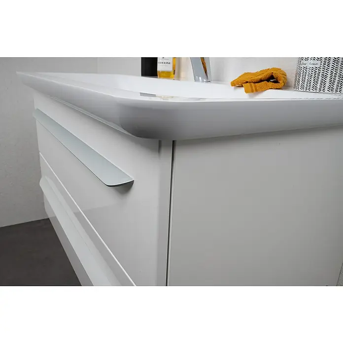 Lanzet M9 Waschtischunterschrank89,2 x 48,9 x 48 cm, Dark Oak - Nahaufnahme eines weißen Waschtischunterschranks mit einer langen silbernen Schubladenleiste. Das moderne Design wird durch ein Waschbecken ergänzt.