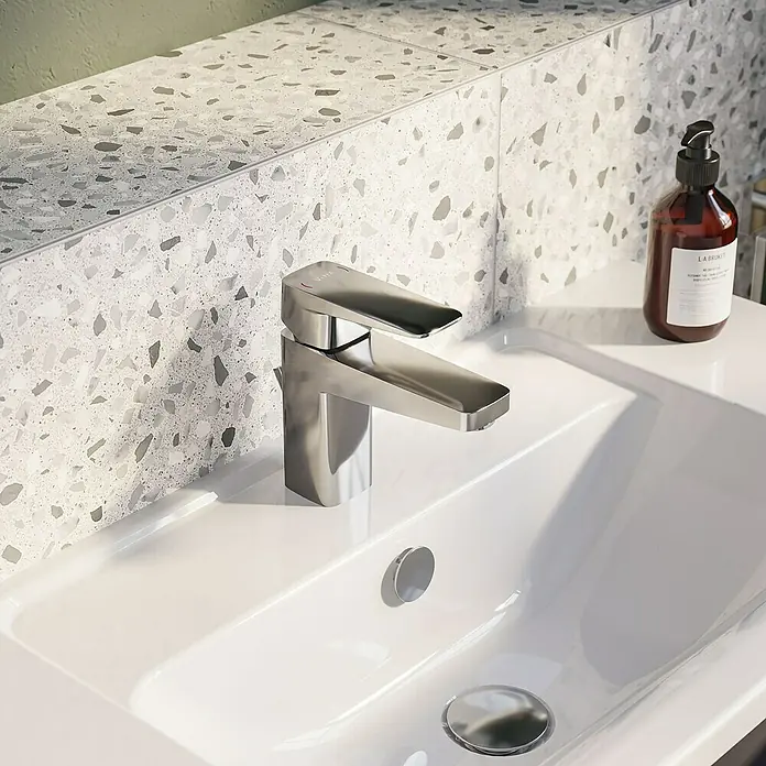 VitrA Waschtischarmatur Root Square - Chrom - Nahaufnahme einer modernen Armatur auf einem weißen Waschbecken mit Terrazzo-Fliesen im Hintergrund.
