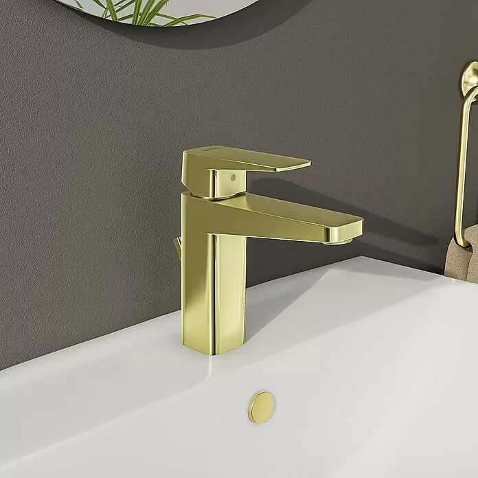 VitrA Überlaufrosette - Gold, Passend für: Waschtische mit rundem Überlaufloch - Gebürsteter goldener Einhebel-Waschtischmischer mit passendem Abflussstopfen in einem weißen Waschbecken.