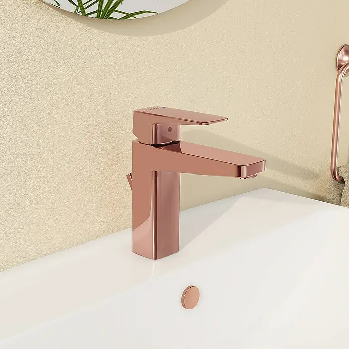 VitrA Waschtischarmatur Root Square - Kupfer - Nahaufnahme eines modernen, roségoldenen Wasserhahns auf einem weißen Waschbecken mit stilvoller Badezimmerdekoration im Hintergrund.