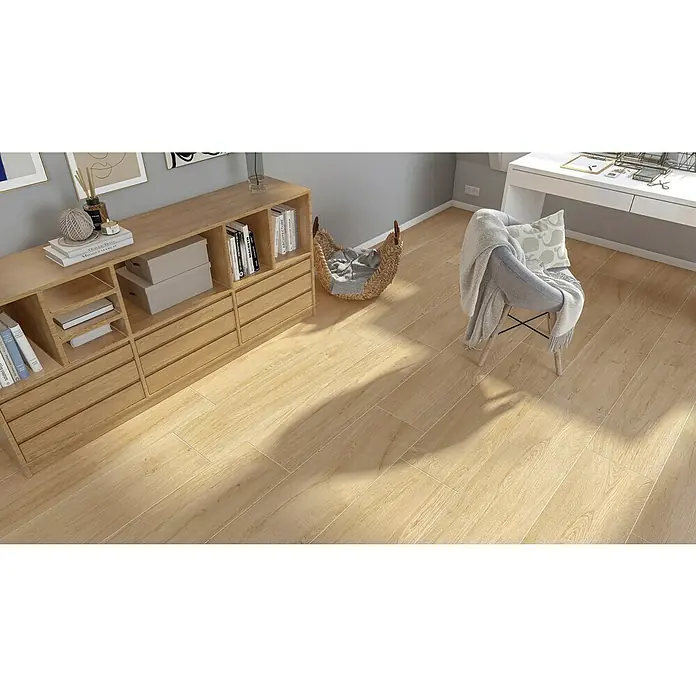 Harmonie by Palazzo Feinsteinzeugfliese - 30 x 120 cm, Eiche Hell, Matt - Ein helles Wohnzimmer mit Holzschrank, geflochtenem Korb und einem Stuhl mit Decke und Kissen, alles auf hellem Holzboden.