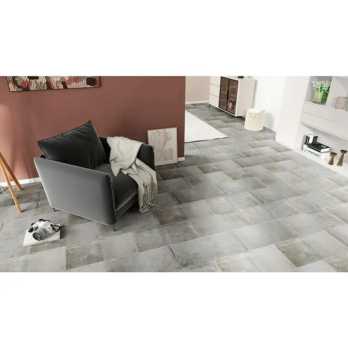 Feinsteinzeugfliese Urban Beton - 30 x 60,4 cm, Grau, Matt - Ein gemütlicher grauer Sessel mit weichen Kissen und einer Decke in einem stilvollen Raum mit Fliesenboden.